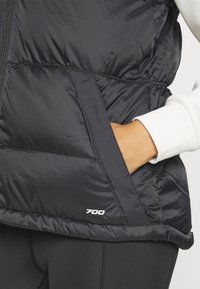 Μαύρο αμάνικο μπουφάν με ανάγλυφο σχέδιο, που διαθέτει τσέπη με φερμουάρ και τον αριθμό "700" τυπωμένο σε λευκό στο τελείωμα. Μαλακή, λαμπερή υφή.