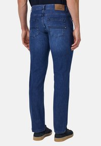 Pantalones vaqueros de denim azul oscuro con un corte recto, que cuentan con dos bolsillos traseros, un parche con el logo en la waistband y detalles de costura sutiles.