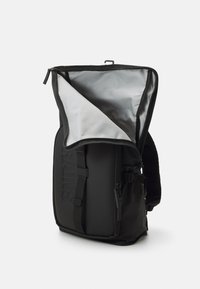 Schwarzer Rucksack mit einem minimalistischen Design, aus strapazierfähigem Material gefertigt. Verfügt über ein graues Innenfutter, einen Reißverschluss, verstellbare Seitenträger und ein Logo-Detail.