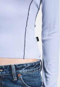 Light blue ribbed long-sleeve top with contrasting dark stitching, paired with high-waisted blue denim jeans showing a visible tag.