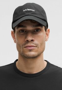 Fekete baseball sapka fehér "lululemon" logóval; egy fekete környakú pólót viselő személyen, a háttér semleges szürke.