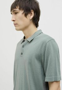 Polo shirt en coton vert avec un col classique, des manches courtes, une patte de boutonnage à trois boutons et une finition douce et texturée.
