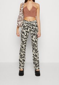 Kobieta ubrana w brązowy krótki top na halter, czarne i białe spodenki w wzory, czarne buty na platformie oraz pasującą torebkę na ramię w ten sam wzór.