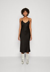 Robe slip en satin noir avec des fines bretelles, longueur midi et texture lisse ; assortie à des bottes en cuir argentées montantes.