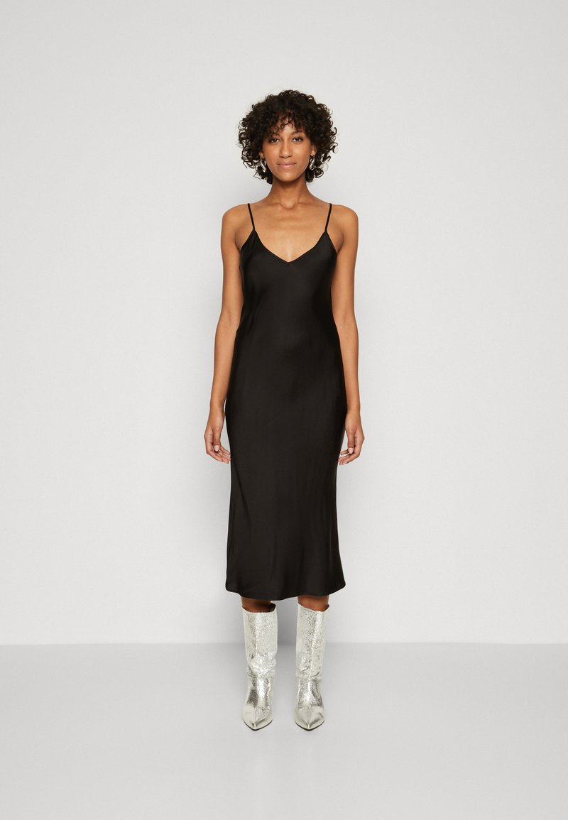 Robe slip en satin noir avec des fines bretelles, longueur midi et texture lisse ; assortie à des bottes en cuir argentées montantes.