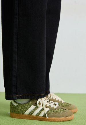 Grønne vævede sneakers med hvide striber, suede detaljer og en gummisål, parret med sorte denim bukser.