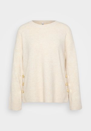 Kremfarget genser med ribbestrikket kant og brede ermer. Har dekorative gullknapper på den ene siden for ekstra detaljer. Myk tekstur.