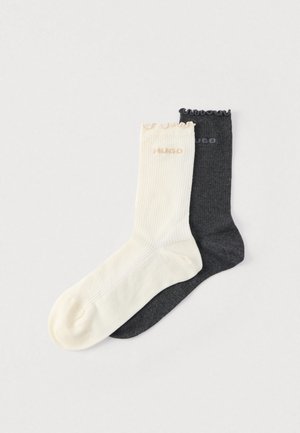 Kaks paari soonikvarbaid: üks beežikas-valge lamedate servade ja logoga, teine tumehall lihtsa disaini ja logoga.