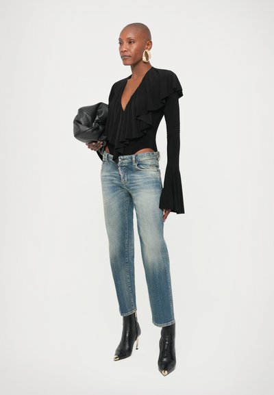 Γυναίκα που φοράει μαύρο μακρυμάνικο τοπ με βολάν, ξεβαμμένο μπλε τζιν, μαύρες μπότες με τακούνι, μεγάλα χρυσά στεφάνια στα αυτιά, κρατώντας μαύρο δερμάτινο τσαντάκι.