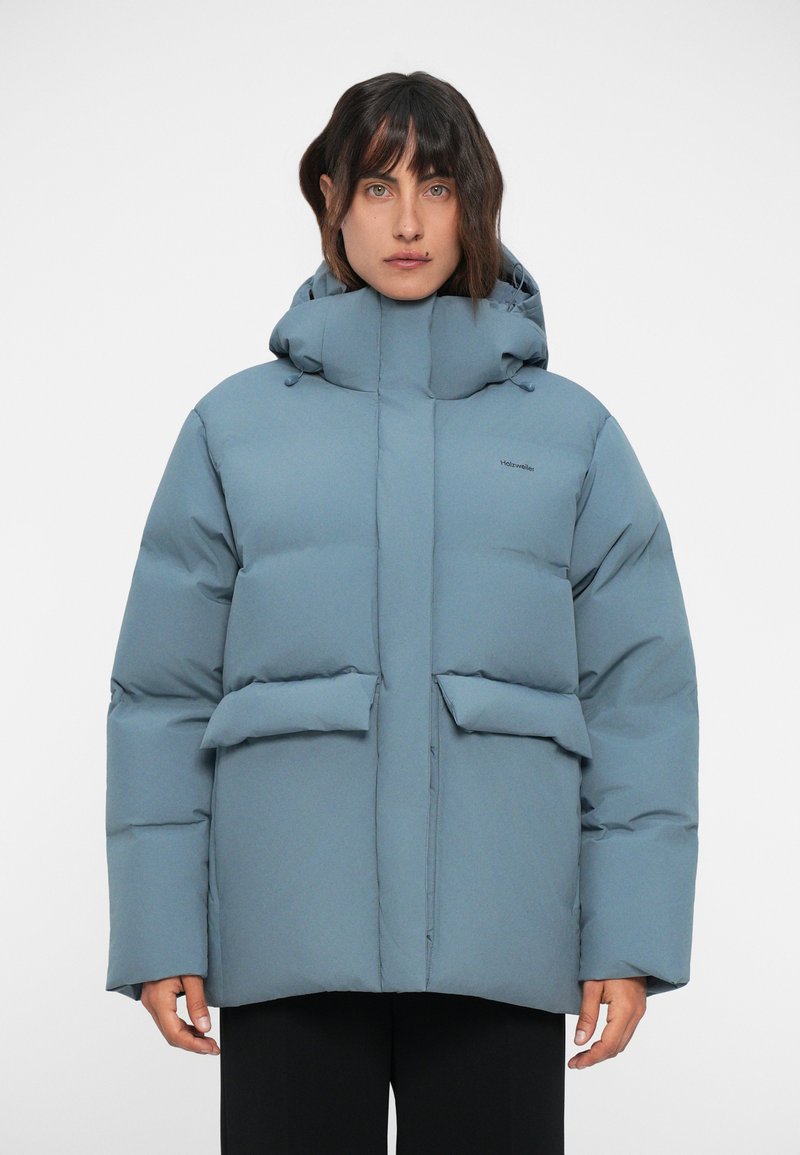 Podložena, kapucijska jakna iz mehkega modrega blaga. Ima velike sprednje žepe in zadrgo. Gladka struktura s sleek, modernim dizajnom.