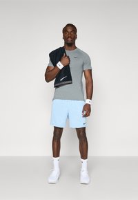 Light grey athletic T-shirt with short sleeves, paired with light blue textured shorts. Accessories include a black towel and white wristbands.