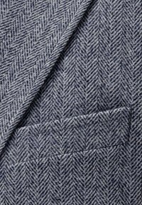 Grau-navy Fischgrätstoff mit glatter Textur, verfügt über ein gefaltetes Revers und ein kleines Taschendetail.