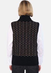 Svart strikket vest med høy ribbestrikket krage, med et mønster i krem og beige, båret over en hvit skjorte. Teksturert overflate.