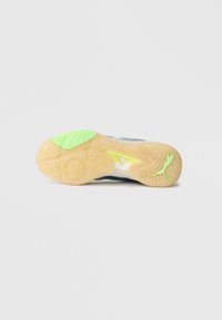 Podeszwa buta sportowego o strukturze jodełki, z jasnobrązową bazą, zielonymi akcentami i logo. Teksturowana, zapewniająca przyczepność i chwyt.