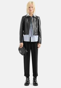 Giacca di pelle nera su una camicia azzurro chiaro, abbinata a pantaloni neri larghi e stivali neri lucidi. Tiene una piccola borsa nera con logo.