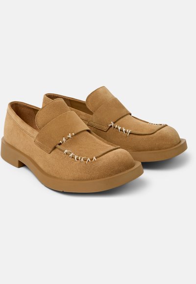 Par af lysebrune ruskindslædersko med tykke gummisåler og hvide dekorative sting på en hvid baggrund.