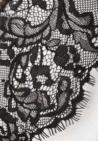 Black lace fabric featuring intricate floral and leaf patterns, with fine details and a textured appearance. Edges are scalloped with fringe accents.