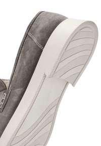 Zapato gris de ante tipo slip-on con suela plana de goma blanca y un patrón de relieve; costuras visibles a lo largo de la costura superior.