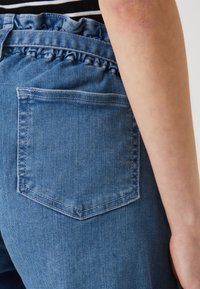 Jeansshorts med ett samlat midjeband och volangdetalj. Har en bakficka med kontrasterande sömmar och en medelblå tvätt.