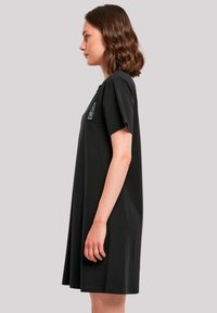 Schwarzes Baumwoll-T-Shirt-Kleid, knielang, lockere Passform, kurze Ärmel. Mit einem dezenten gestickten Design im linken Brustbereich.