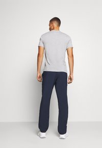 T-shirt cinza de mangas curtas combinado com calças azul-marinho, com um design de corte reto. Modelo usa sapatilhas brancas, visto de trás.