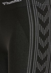 Sorte atletikleggings med grå chevronmønstre og fine prikkede striber, med et hvidt "hummel" logo nær taljen.