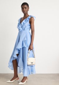 Light blue dress with ruffled sleeves and asymmetrical hem. Matched with white slingback shoes and a cream handbag. Smooth fabric texture.