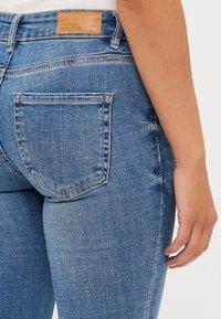 Siniset farkut, joissa on keski-nosto, viiden taskun malli ja suorakulmainen nahkaleima takavyötäröllä.