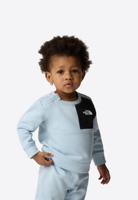 Light blue sweatshirt with a black chest panel featuring a logo. Soft texture, round neckline, long sleeves, and matching pants.