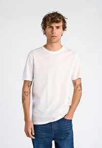 Biały bawełniany t-shirt z okrągłym dekoltem, krótkimi rękawami i luźnym krojem, zestawiony z ciemnoniebieskimi jeansami. Czysty, prosty design.