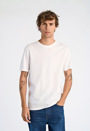 Biały bawełniany t-shirt z okrągłym dekoltem, krótkimi rękawami i luźnym krojem, zestawiony z ciemnoniebieskimi jeansami. Czysty, prosty design.