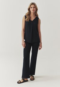 Särgiteta tumesinine blouse, millel on V-kaelus, koos tumedate flared teksade ja mustade sandaalidega, millel on rihm ja kuldne riistvara.