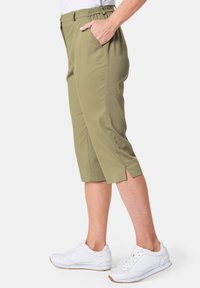 Olivgrüne Capri-Hosen mit lässiger Passform, featuring einen elastischen Bund, Seitentaschen und Schlitze am Saum. Kombiniert mit weißen Sneakern.