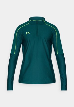 Top sportiv cu mâneci lungi, culoare teal închis, cu guler cu fermoar de un sfert, accente verzi de-a lungul umerilor și textură netedă.