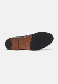 Sole in cuoio marrone con interna color beige con logo impresso, suola in gomma nera liscia e dettagli decorativi lungo i bordi.