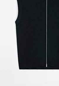 Svart ärmlös topp med en texturerad stickad mönster, med en hel längd silverdragkedja och ribbad fåll, mot en vit bakgrund.