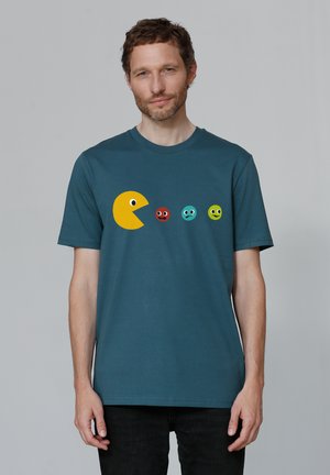 Teal cotton t-shirt featuring a yellow Pac-Man graphic and four colorful ghost faces in red, blue, green, and light green. Short sleeves.