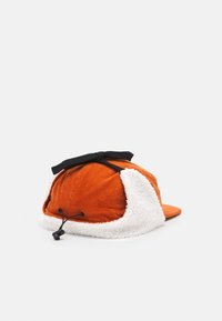Orange corduroy cap with white fluffy lining, black tie detail, and adjustable strap. Features a classic curved brim design.