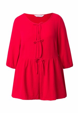 Haut rouge ample en tissu texturé, avec un col rond, des manches trois-quarts et un détail de nouage à l'avant.
