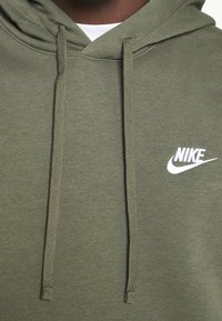 Olivgrön Nike-huvtröja med avslappnad passform, utrustad med en känguruficka, justerbara snören och en vit broderad logotyp på bröstet.