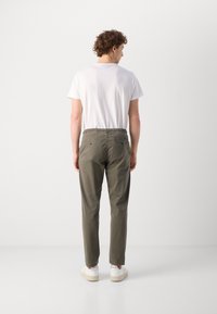 Pantalonii bărbați de culoare verde măsliniu au o talie elastică, buzunare laterale și la spate, și picioare înguste. Purtați cu un tricou alb simplu și adidași albi.