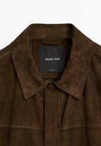 Bruine suède jas met een kraag, details van een knoopsluiting en een zwart label met de tekst "Massimo Dutti" aan de binnenkant van de hals.