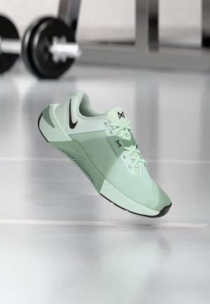 Scarpa sportiva verde chiaro con tomaia in mesh, dettagli neri, suola texturizzata e lacci. Presenta un logo distintivo sulla linguetta e sul lato.