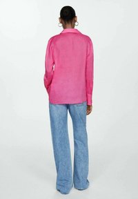 Chemise rose en lin à boutons, manches longues, vue de dos, associée à un jean large bleu clair. Texture lisse, coupe décontractée et design minimaliste.