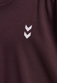 Bordowa tkanina o gładkiej fakturze ma biały logo w kształcie chevronu po lewej stronie, podkreślając minimalistyczny design.