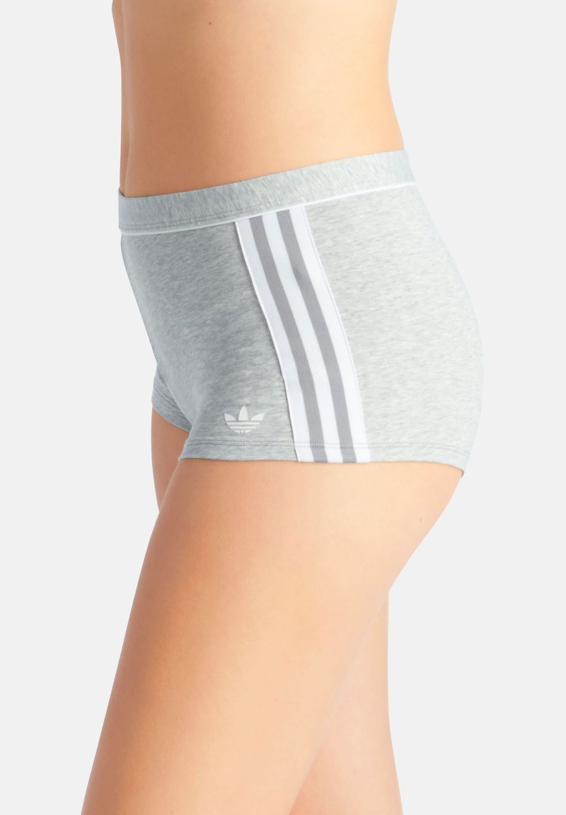 Primo piano di una persona che indossa pantaloncini da sport grigio chiaro con tre strisce bianche e un logo Adidas sul lato.