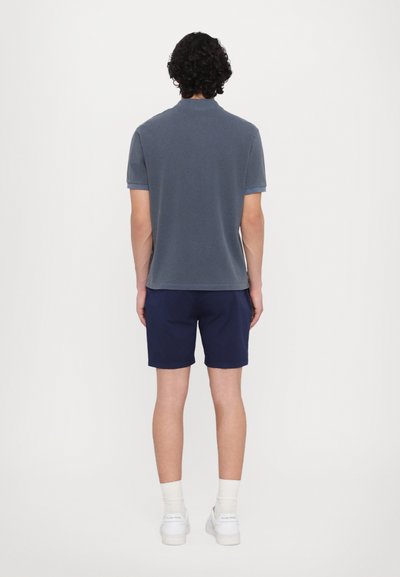 Polo shirt da uomo di colore blu navy realizzato in cotone, presenta maniche corte, colletto classico e orlo dritto. Indossato con pantaloni corti coordinati.