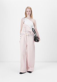 Lyserøde jumpsuits med brede ben, justerbare stropper og forlommer. Sammen med en hvid top med én skulder og en sort håndtaske.