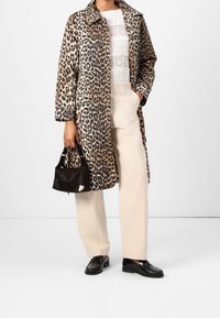 Femme portant un manteau à imprimé léopard, un haut blanc texturé, un pantalon beige, des mocassins noirs, tenant un petit sac à main noir à texture en fourrure.