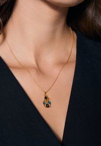 Złoty naszyjnik z delikatnym łańcuszkiem i wisiorkiem z trzema kolorowymi kamieniami: ciemnoniebieskim, jasnoniebieskim i czarnym, w kształcie kropli.